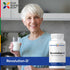Elderly woman smiling as she holds a glass of milk, standing beside a bottle of Revolution-D.